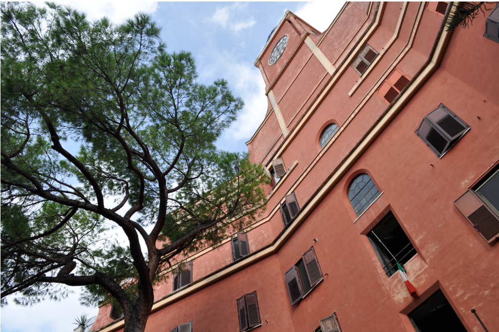 Kuvassa roomalainen poltetun oranssin värinen kaunis vanha kerrostalo ja sen edessä kasvava puu sammakkoperspektiivistä.