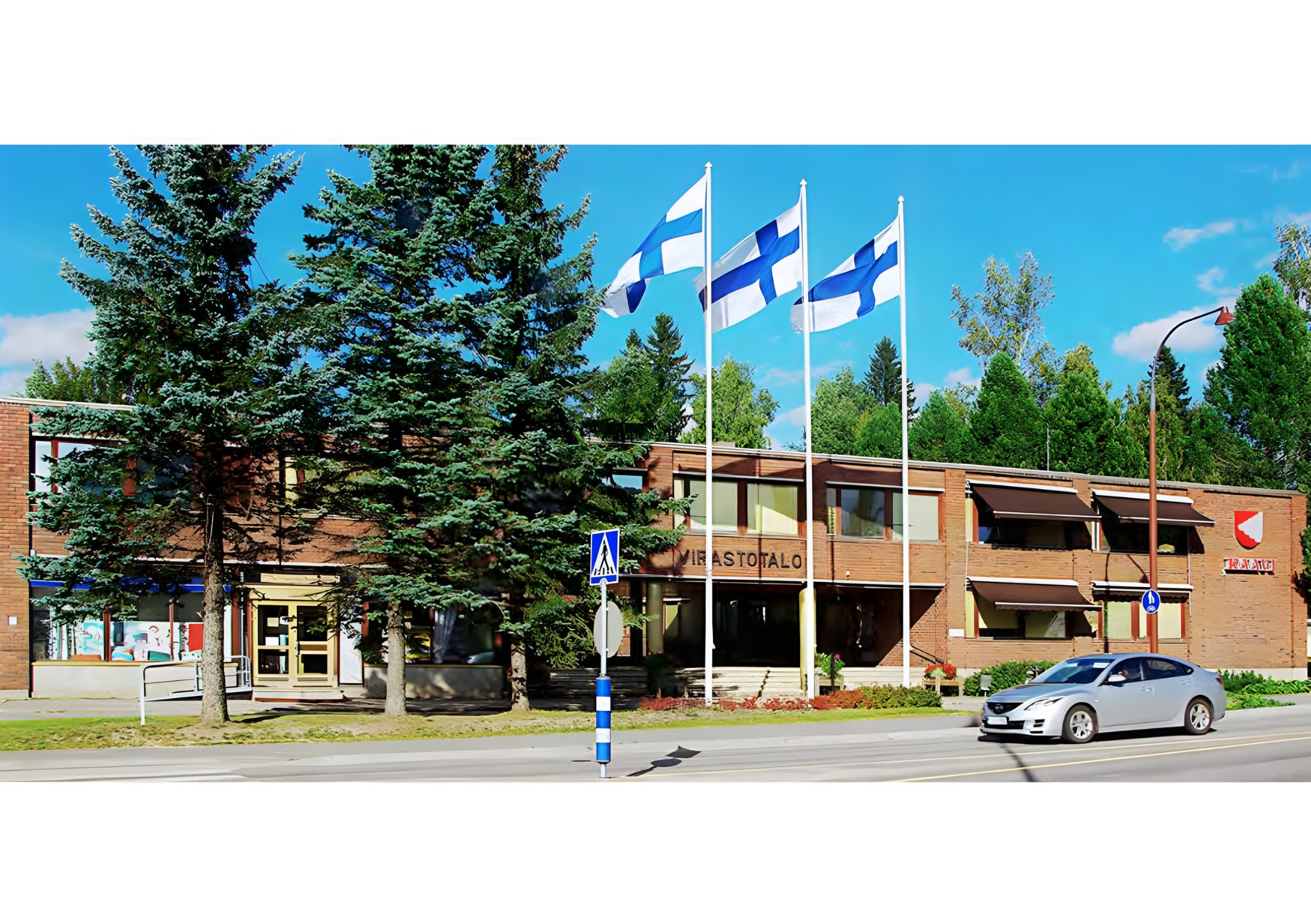 Kesäinen kuva Kaavin kunnantalosta, jonka edustalla liehuu kolme Suomen lippua.